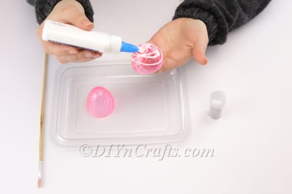 Applying glue to the plastic Easter egg.