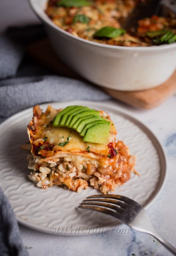 Enchilada casserole with avocado toppings served in a plate.