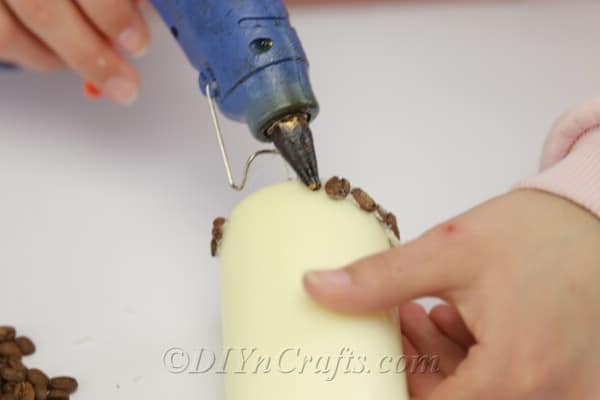 Using hot glue to attach coffee beans to candle