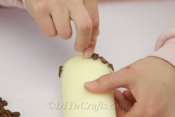 Placing coffee beans on a pillar candle with hot glue