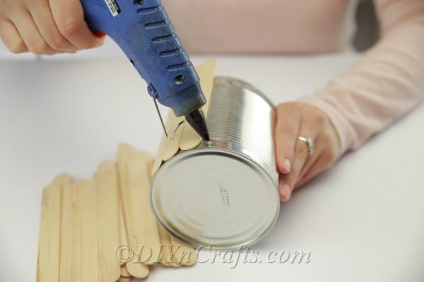 Gluing popsicle sticks onto the outside of the empty can