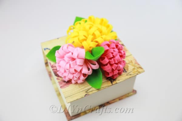 DIY fabric flowers in red, yellow, and pink with added leaves.