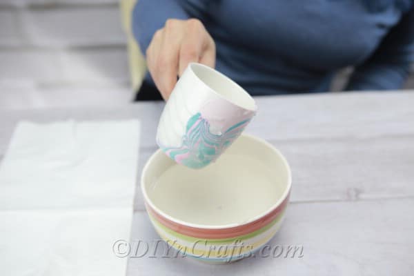 Dipping a white coffee cup into bowl of water and nail polish