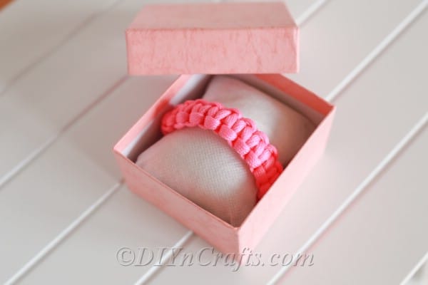 A finished pink square knot bracelet friendship bracelet sitting in a pink and white jewlery box that is sitting on a white surface