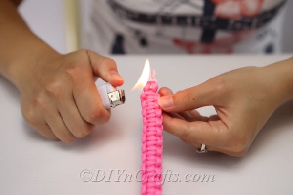Burning the ends of the thread on the square knot bracelet with a lighter to secure
