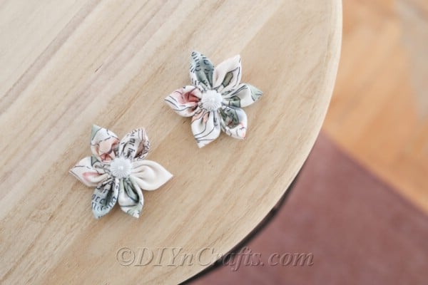 Two completed fabric flowers displayed on a wood table.
