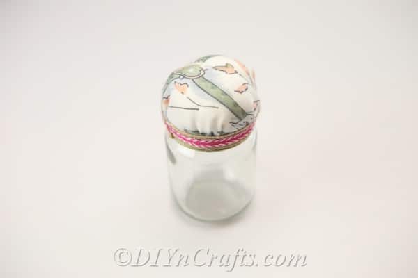 A completed pincushion jar rests on a surface.