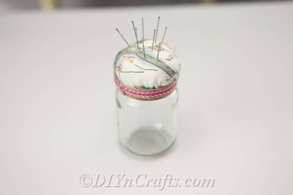 A completed pincushion jar with pins stuck in it sitting on the table.