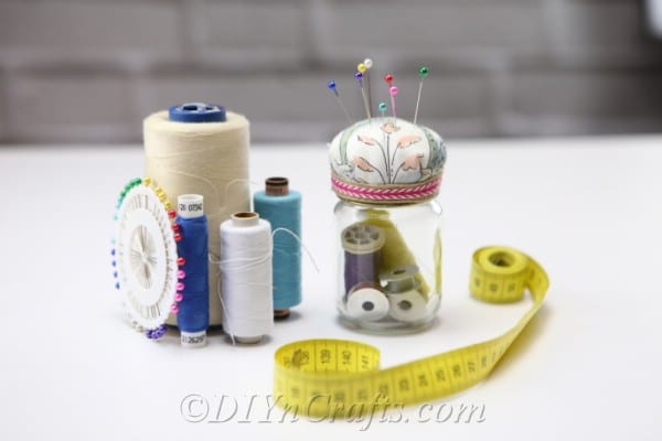 A pincushion jar displayed with other sewing materials.