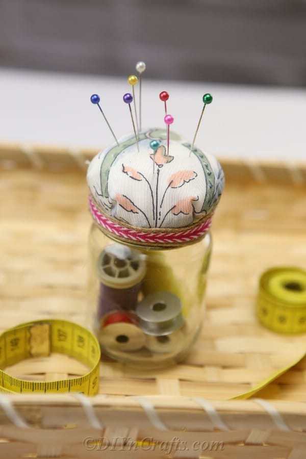 A completed pincushion jar together with sewing supplies in a basket.