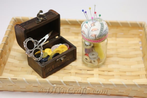 A pincushion jar and other sewing materials in a tray.