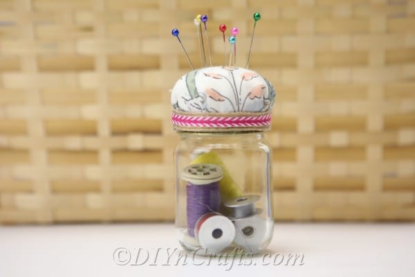 A completed pincushion jar with a basket in the backdrop.