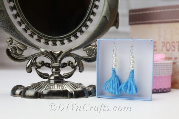 Tassel earrings hang in a box displayed next to an ornate mirror.
