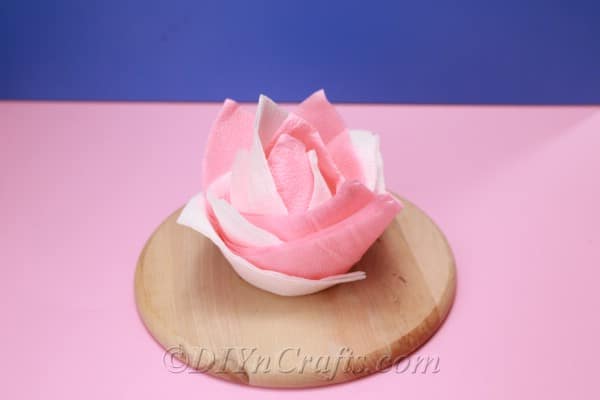Completed pink and white napkin after watching how to fold napkins tutorial sitting on a round wooden board on a pink surface