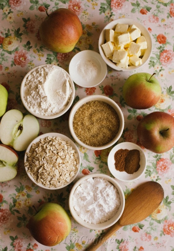 Ingredients for apple crumble recipe in small white bowls on floral tablecloth