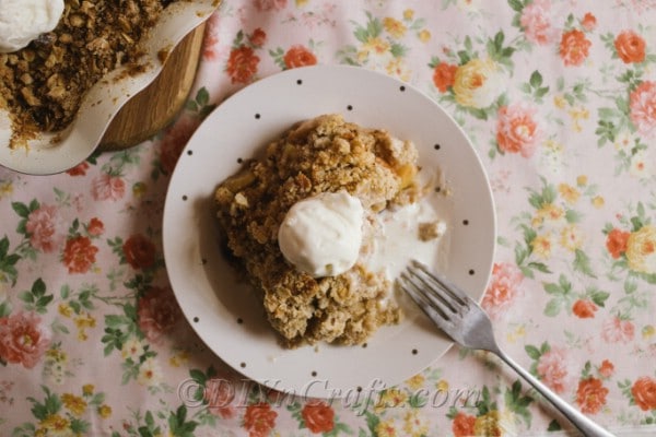 Overhead picture of a bowl of apple crumble sitting on a floral tablecloth