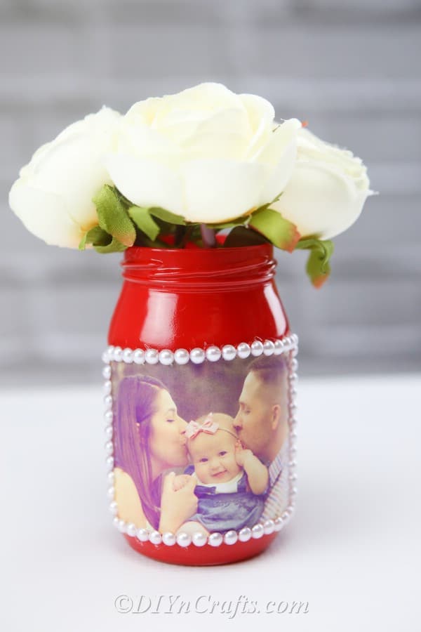 A handmade photo jar vase featuring a family photo displayed with a wall in the background.