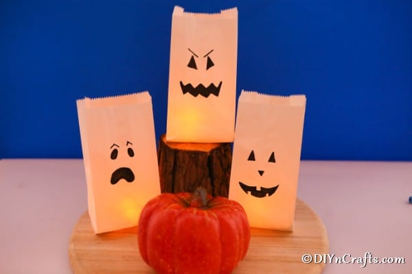 A trio of halloween ghost luminary bags lit and sitting in front of a blue background