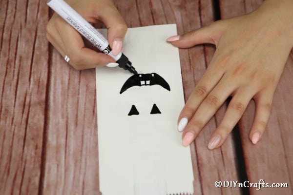 A smiling face being drawn onto a luminary bag for Halloween
