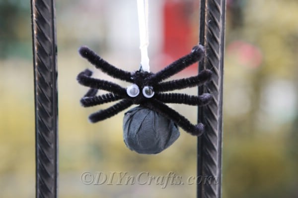 Halloween lollipop spider craft hanging from a black metal fence outside