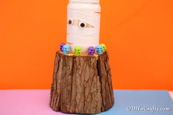 A completed mason jar lights halloween mummy sitting on top of a wooden block surrounded by colorful skulls