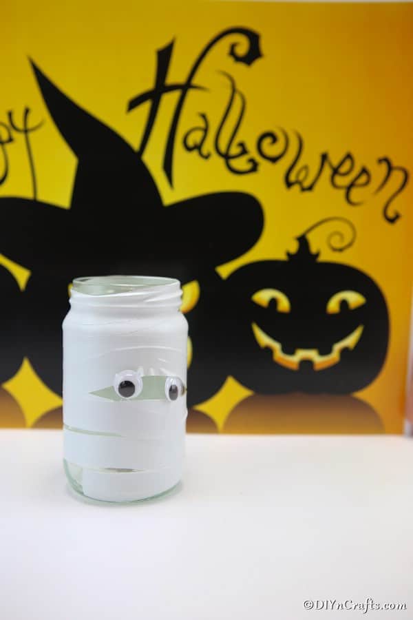 Mason jar lights halloween mummy sitting on white counter with yellow halloween sign in background