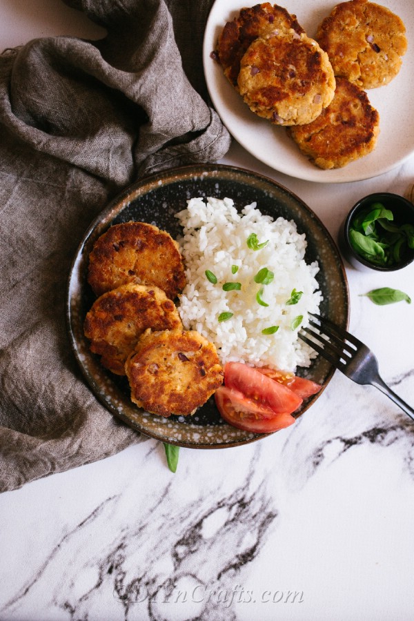 An overhead picture of a salmon patty recipe on a plate with rice and tomatoes