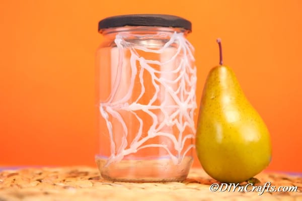 A completed halloween spider web jar sitting on a brown surface with orange background