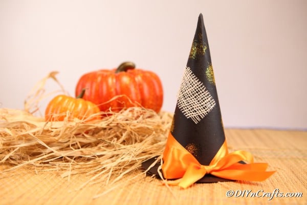 Witch hat displayed on brown cloth next to mini pumpkins