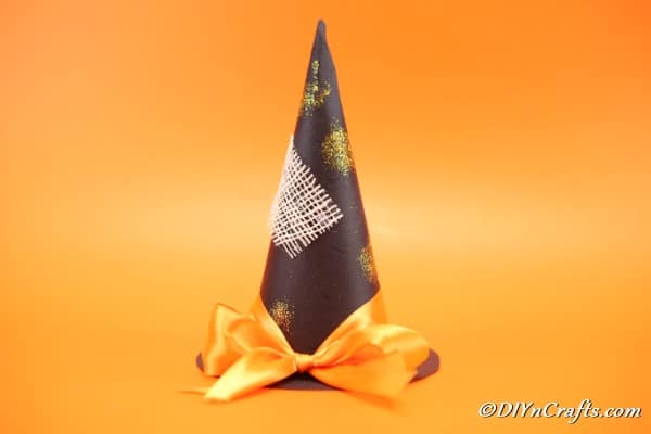 A finished witch hat halloween decoration sitting on a n orange background and surface