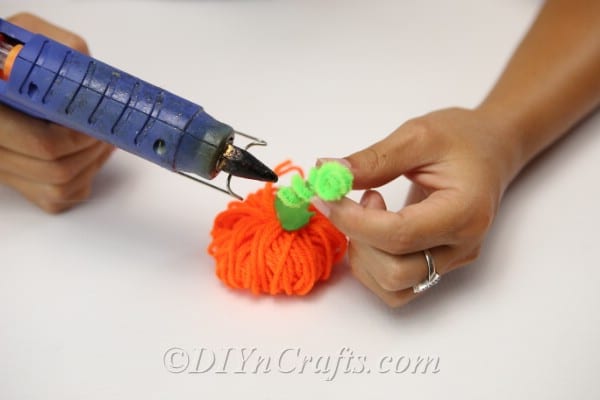 A woman hot gluing the leaves and stem to the top of the yarn pumpkin