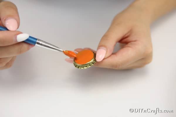 Painting a bottle cap orange for a pumpkin magnet