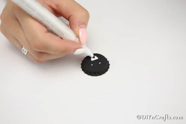 Drawing a face on a black bottle cap to create a spider