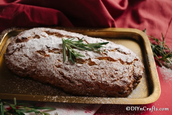 A loaf of christmas stollen on a baking sheet topped with sugar and herbs