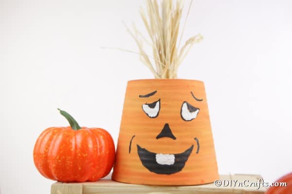 A finished pumpkin planter sitting on a wooden box with a small decorative pumpkin on the side