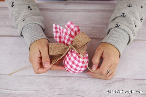 Tying a burlap bowl onto a checkered fabric Christmas tree ornament