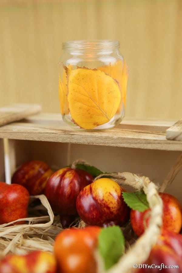 A wooden box of apples with a fall leaf candle lanterns craft sitting on top