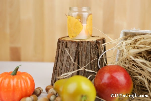 A single fall leaf candles lantern sitting on a small wooden stump surrounded by fall decorations
