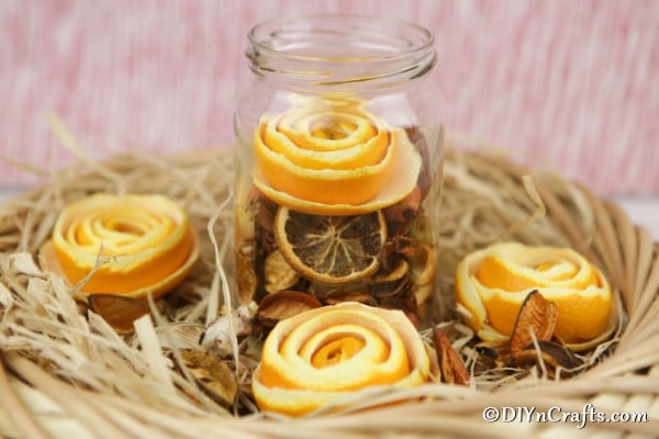 Orange flowers in a glass jar surrounded by decorative hay and flowers