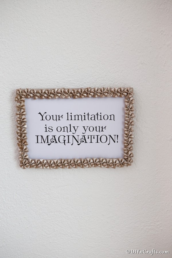 A macaroni art picture frame hanging on a white wall