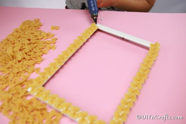 Adding pasta to a picture frame with hot glue