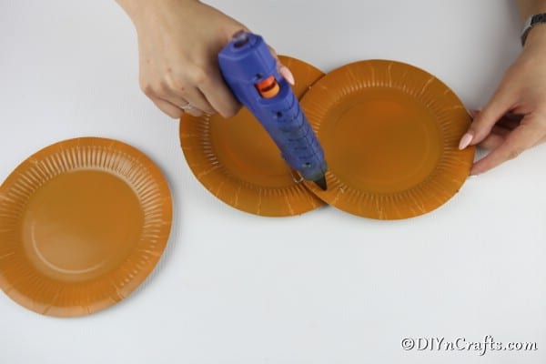 Gluing the plates together to create a paper plate pumpkin
