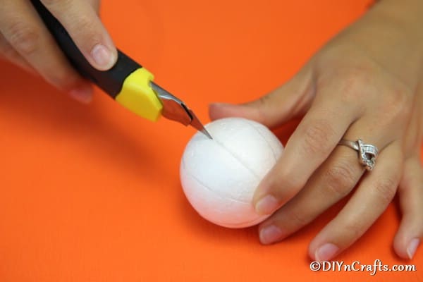 Cutting the styrofoam ball with craft knife for pumpkin ornament