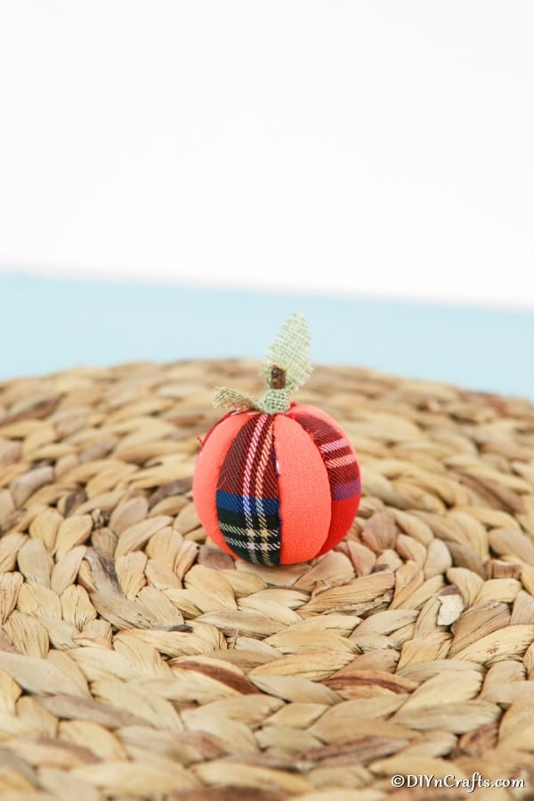 A pumpkin ornament covered in scrap fabric sitting on a woven mat