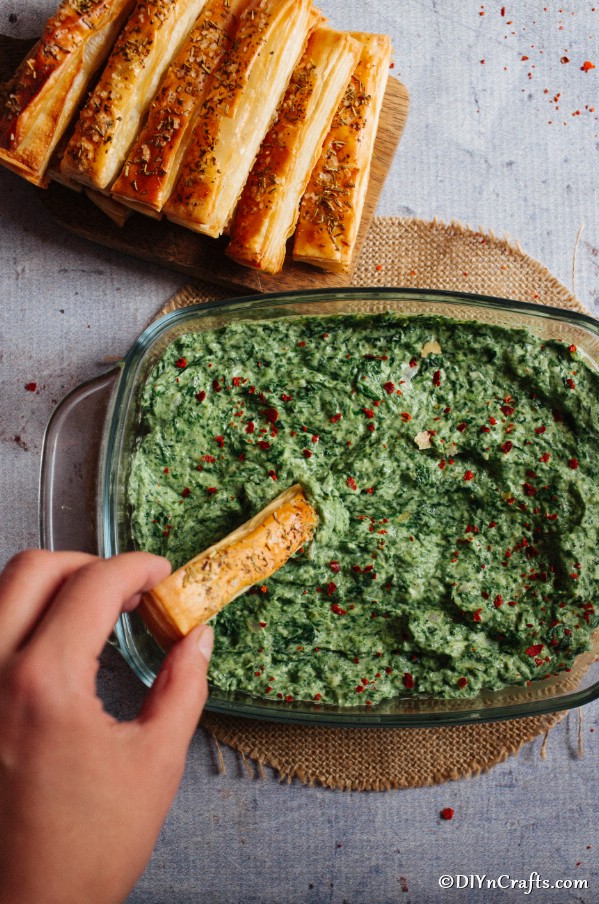 A hand holding a breadstick dipping into the hot spinach dip
