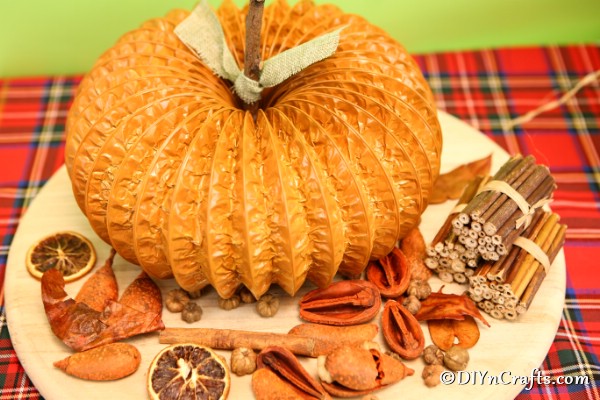 Dryer vent pumpkin sitting on a wooden board with fall decor items beside it