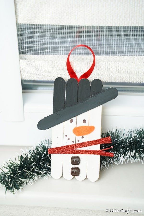 A snowman popsicle stick ornament leaned against a windowsill