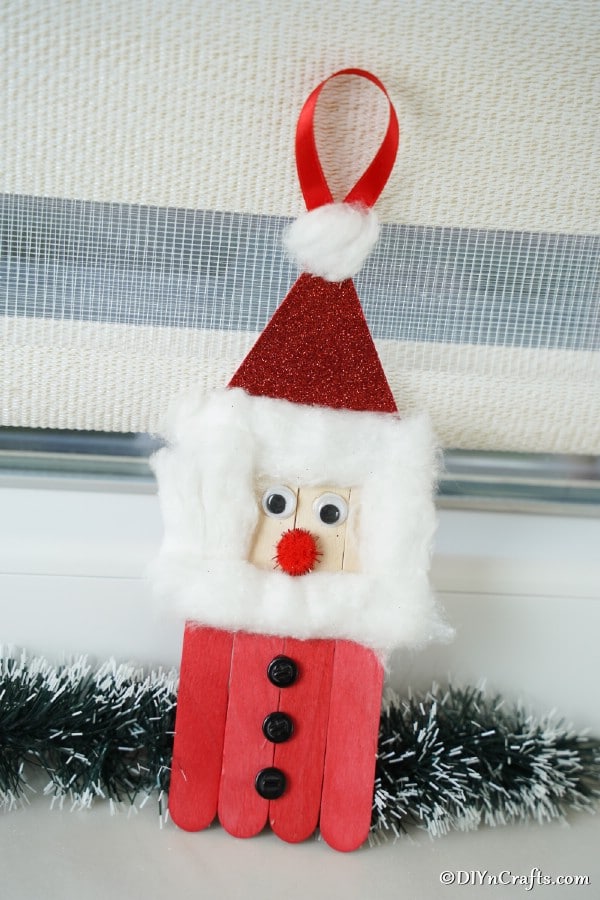 A craft stick Santa ornament sitting on a windowsill