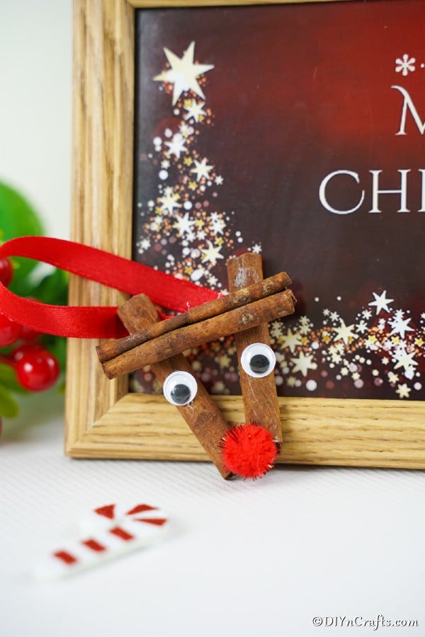 Cinnamon stick reindeer ornaments propped against a holiday sign