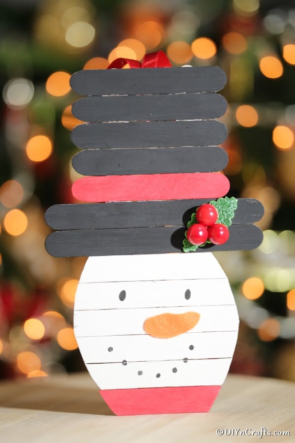Up close picture of a craft stick snowman in front of a Christmas tree